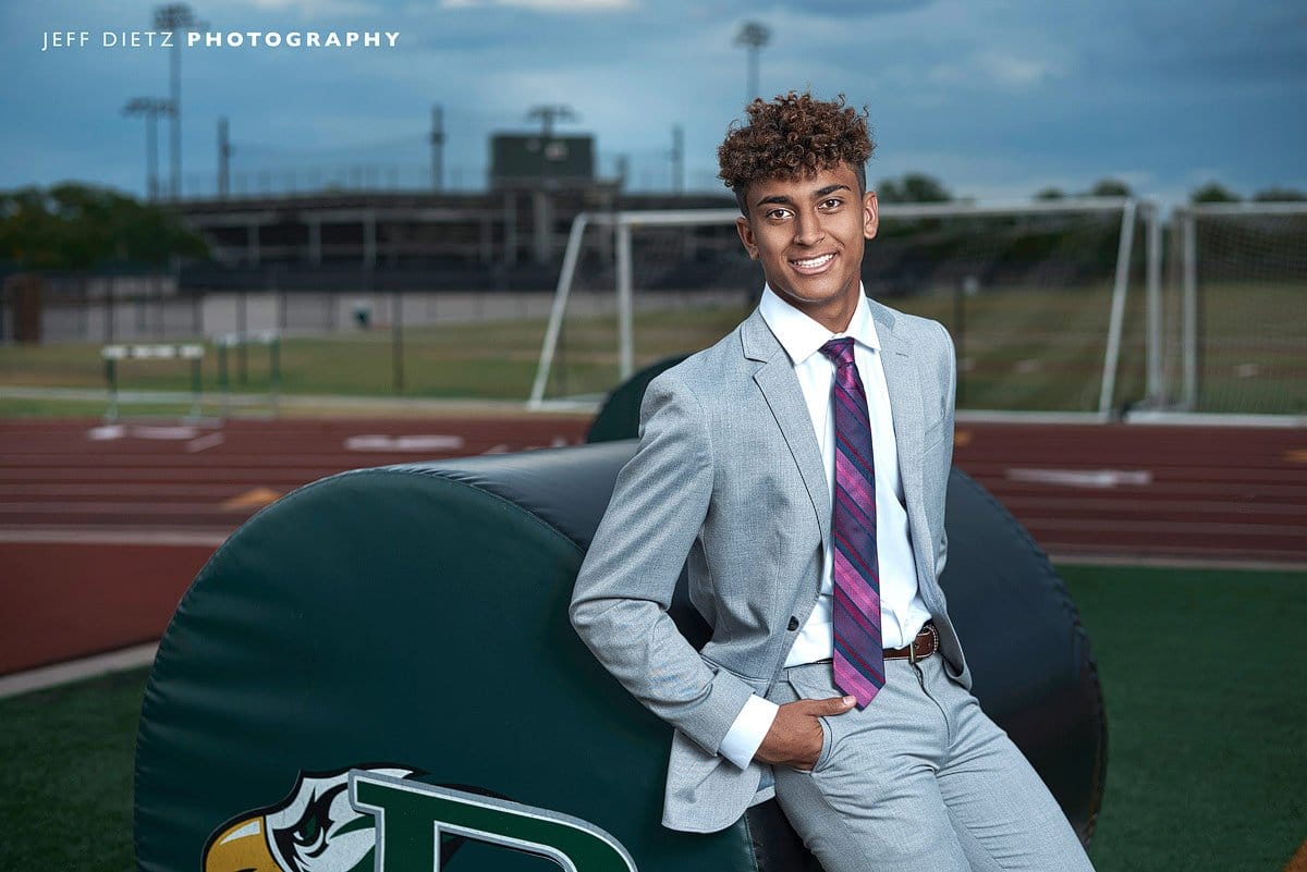 prosper high school football player poses by green practice pads for senior photos