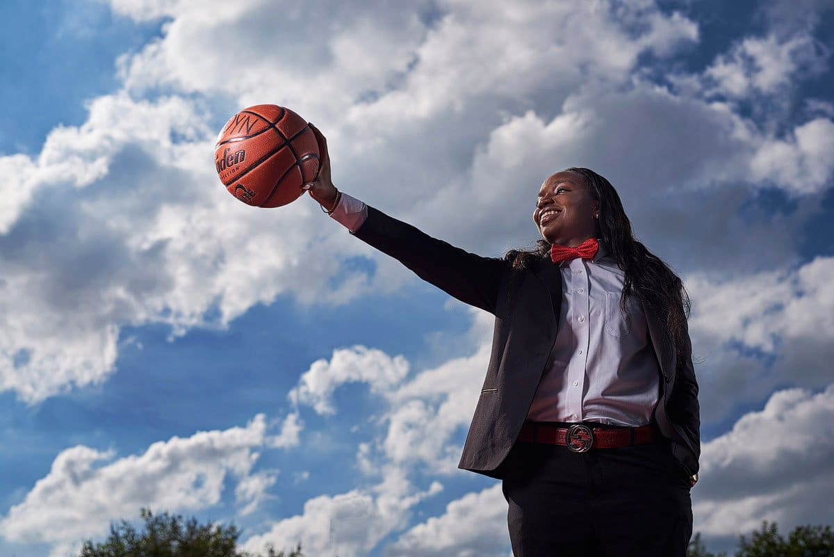 prosper girls basketball player palms ball in hand wearing a suit in front of clouds