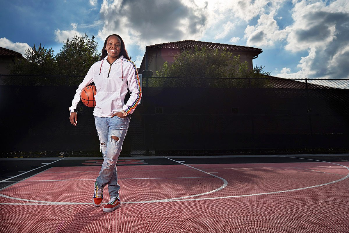 prosper girls basketball player for senior portraits on outdoor court holds ball in arms