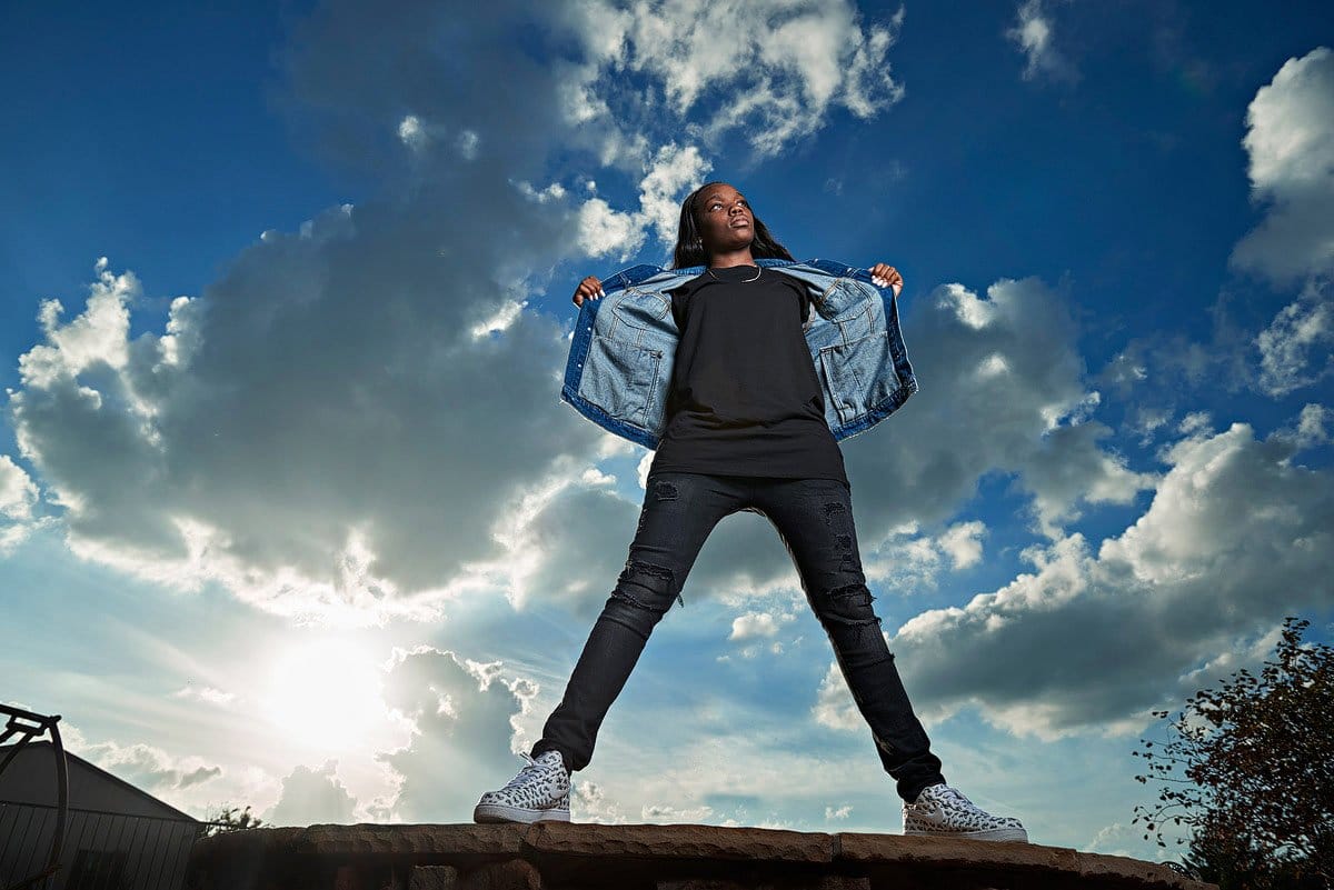 prosper girls basketball player stand on rock for senior portraits with jean jacket open