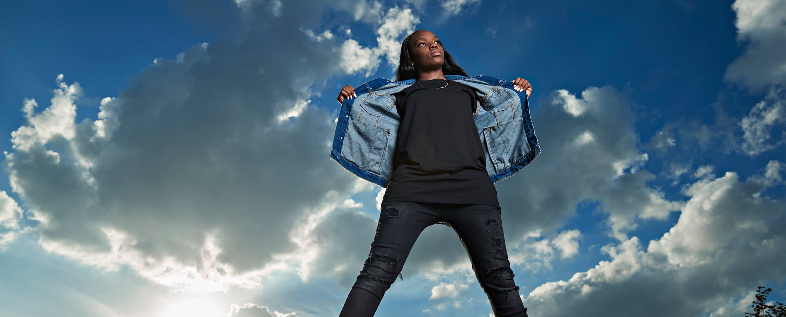 prosper girls basketball player Oliver wears a jean jacket for senior pictures with blue sky