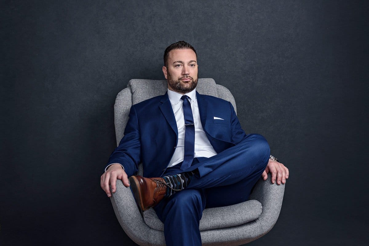 dallas lawyer headshots in a blue suit legs crossed in gray chair frisco texas