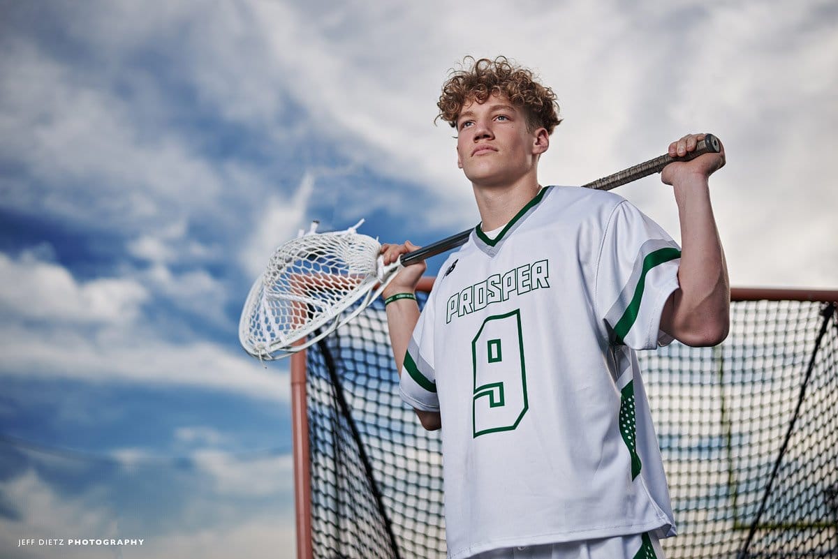 prosper lacrosse goalie poses with stick and blue skies by the net senior portraits