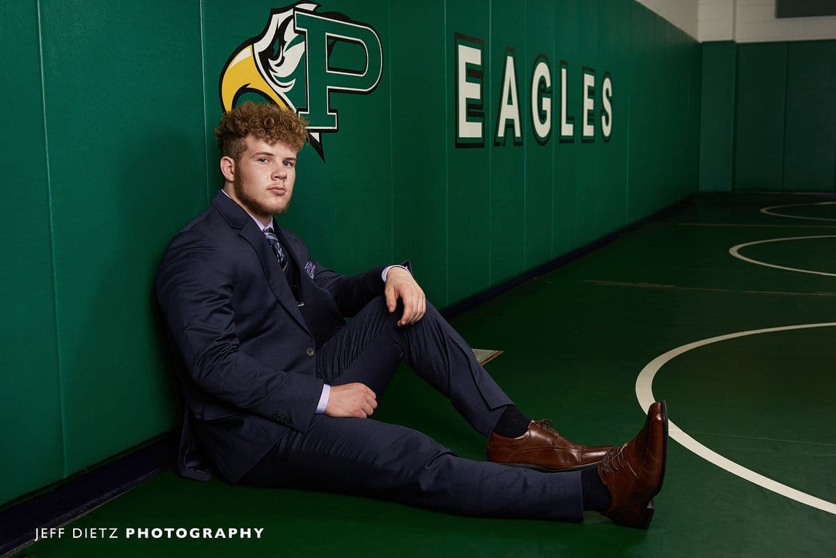 prosper senior wrestler leaning up against the wall in the practice gym for portraits