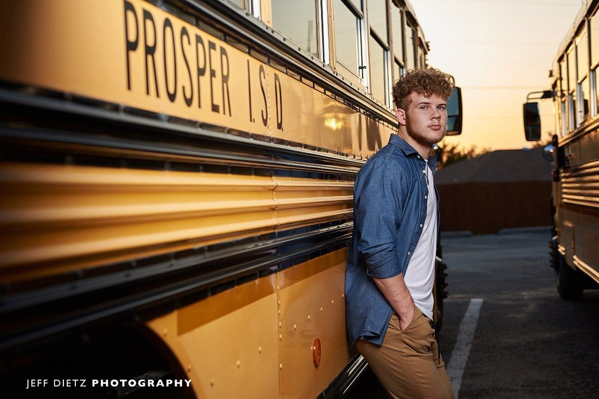 prosper senior stands next to school bus for senior pictures