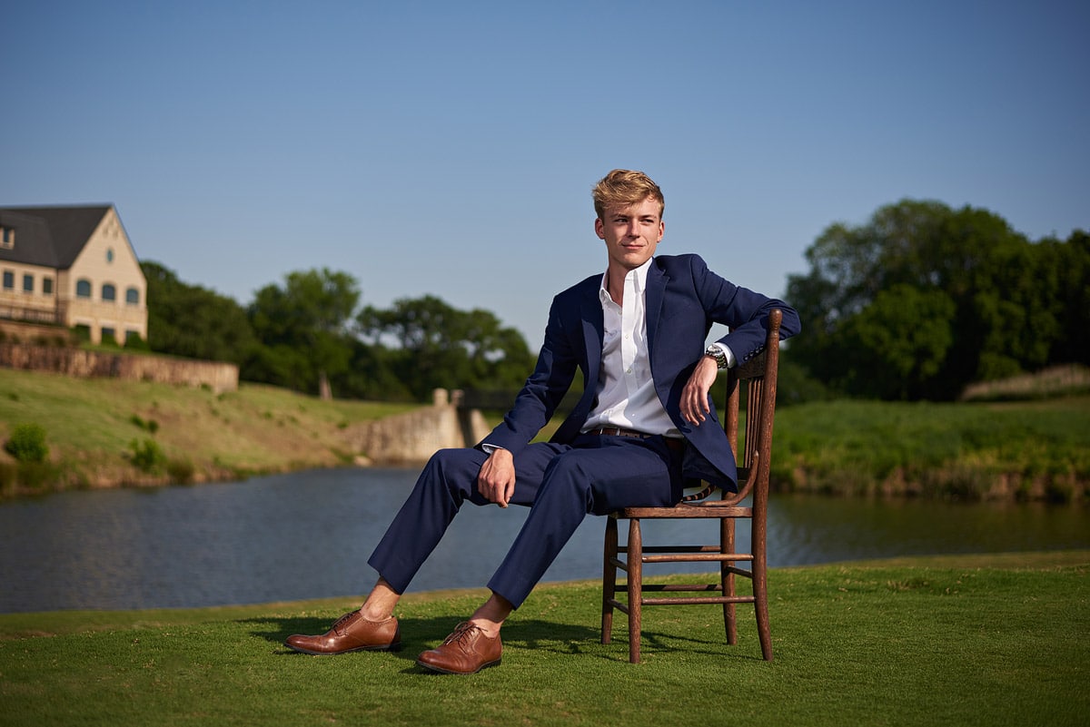 southlake senior sits in wooden chair on the golf course in a suit