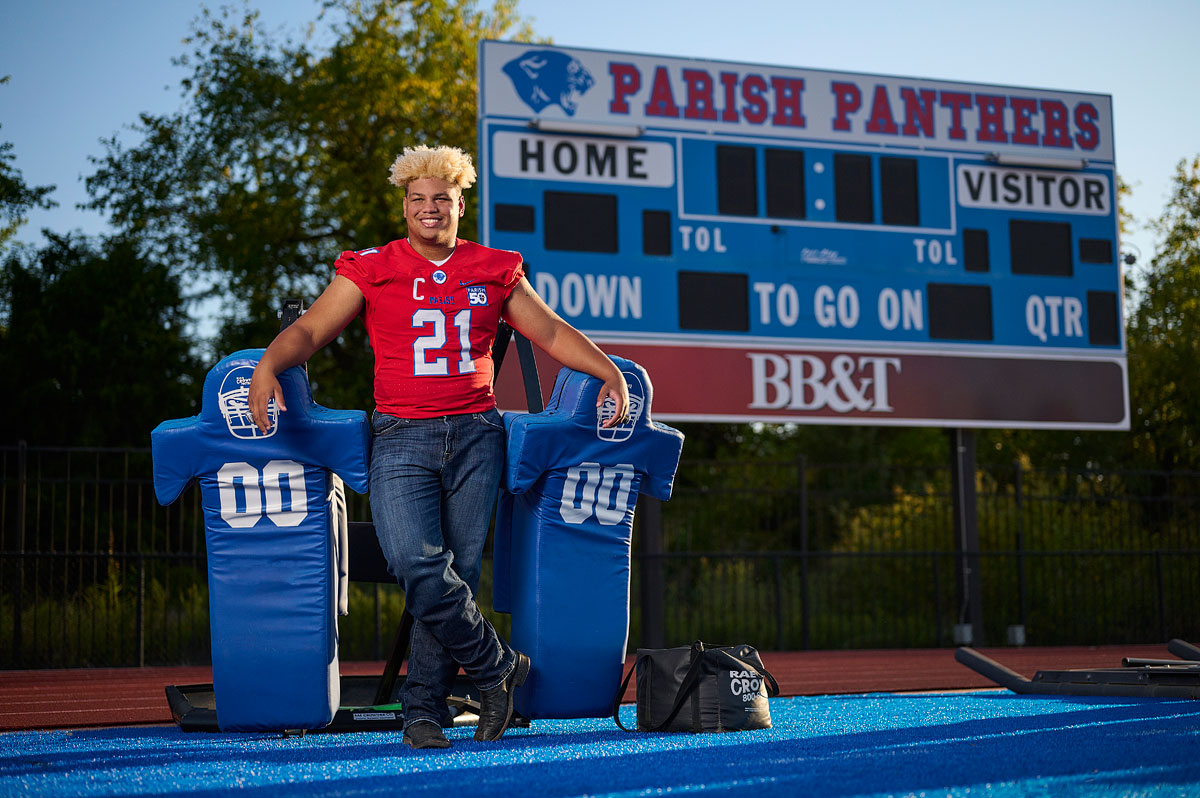 parish episcopal football player stands by practice equipment in front of score board for senior pictures