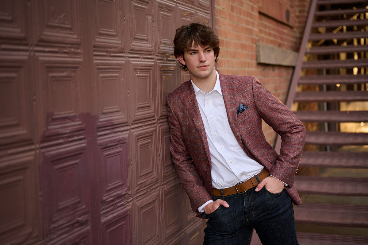 parish episcopal senior leaning against wall for pictures in downtown dallas with a red sports jacket and jeans