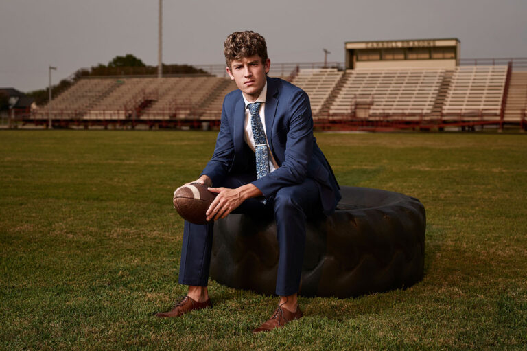 southlake carroll senior sports portraits for football in dragons stadium player sitting on a tire with a football by photographer Jeff Dietz